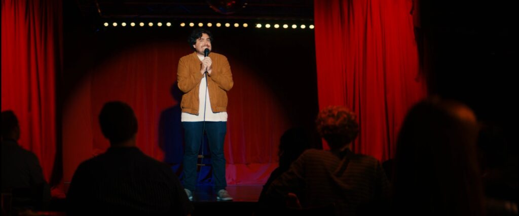 Jack de Senna on stage at comedy club with spotlight in warmly lit scene