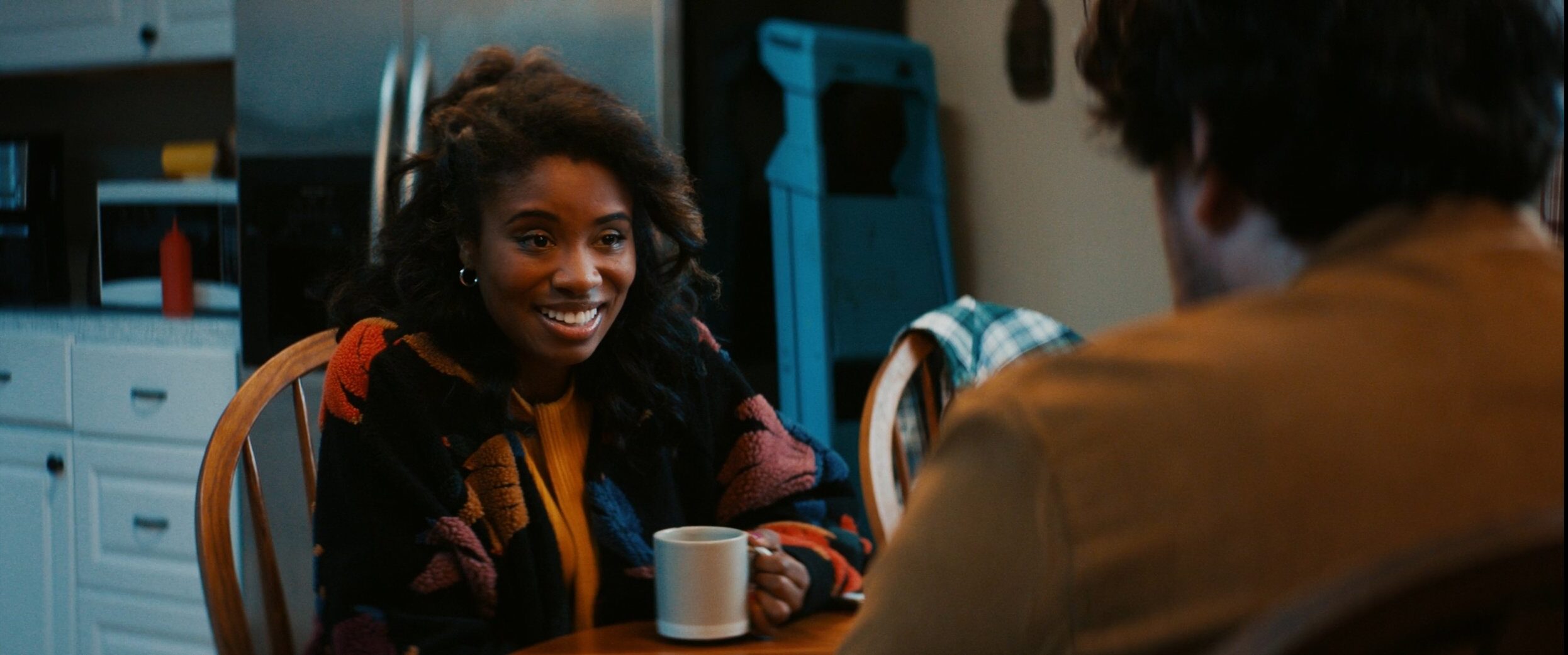 Akilah Hughes sitting at a breakfast table at night with a coffee cup in her hand and smiling