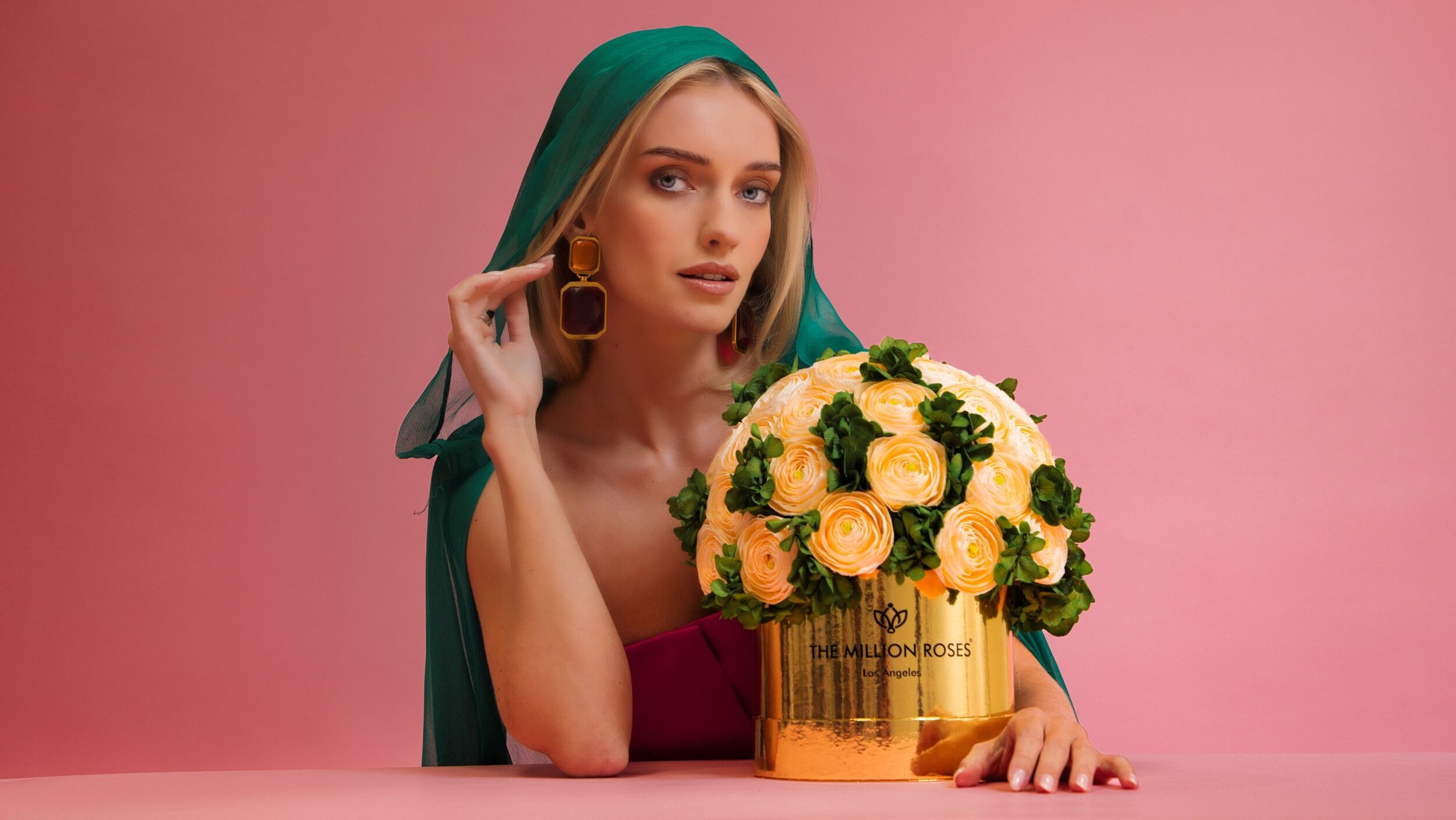 Photo model with green veil presenting yellow The Million Roses flowers in gold box and looking into camera