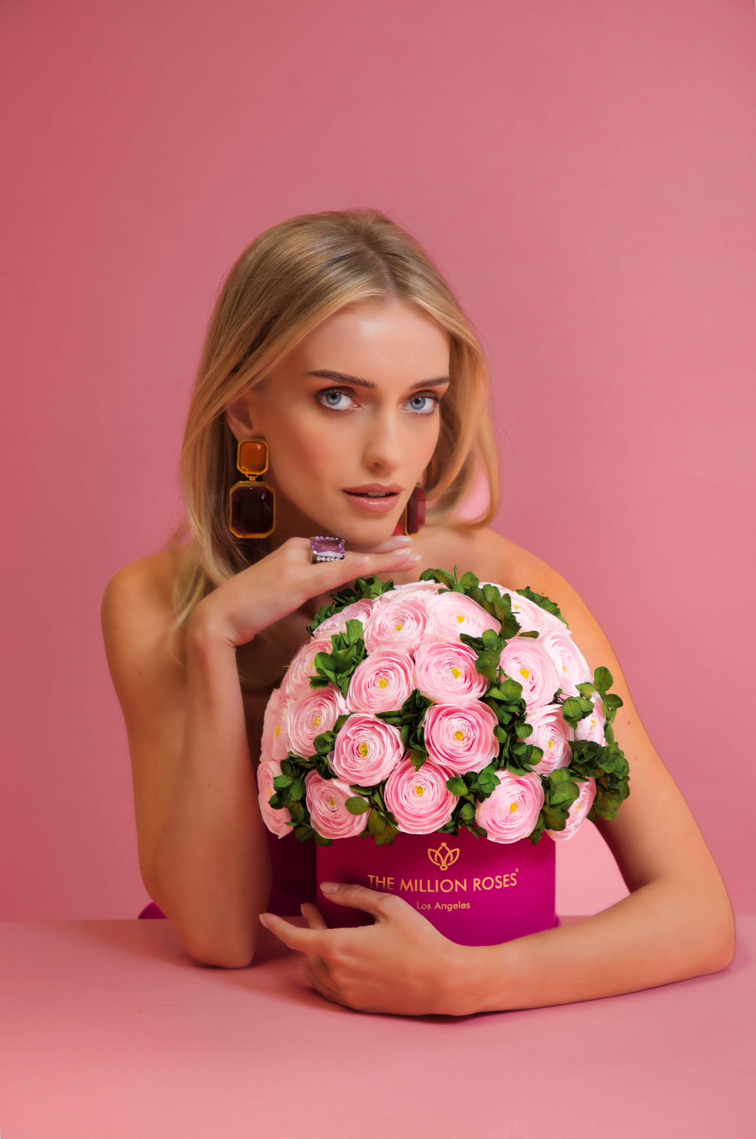 Photo model presenting pink The Million Roses flowers in pink box looking at the camera