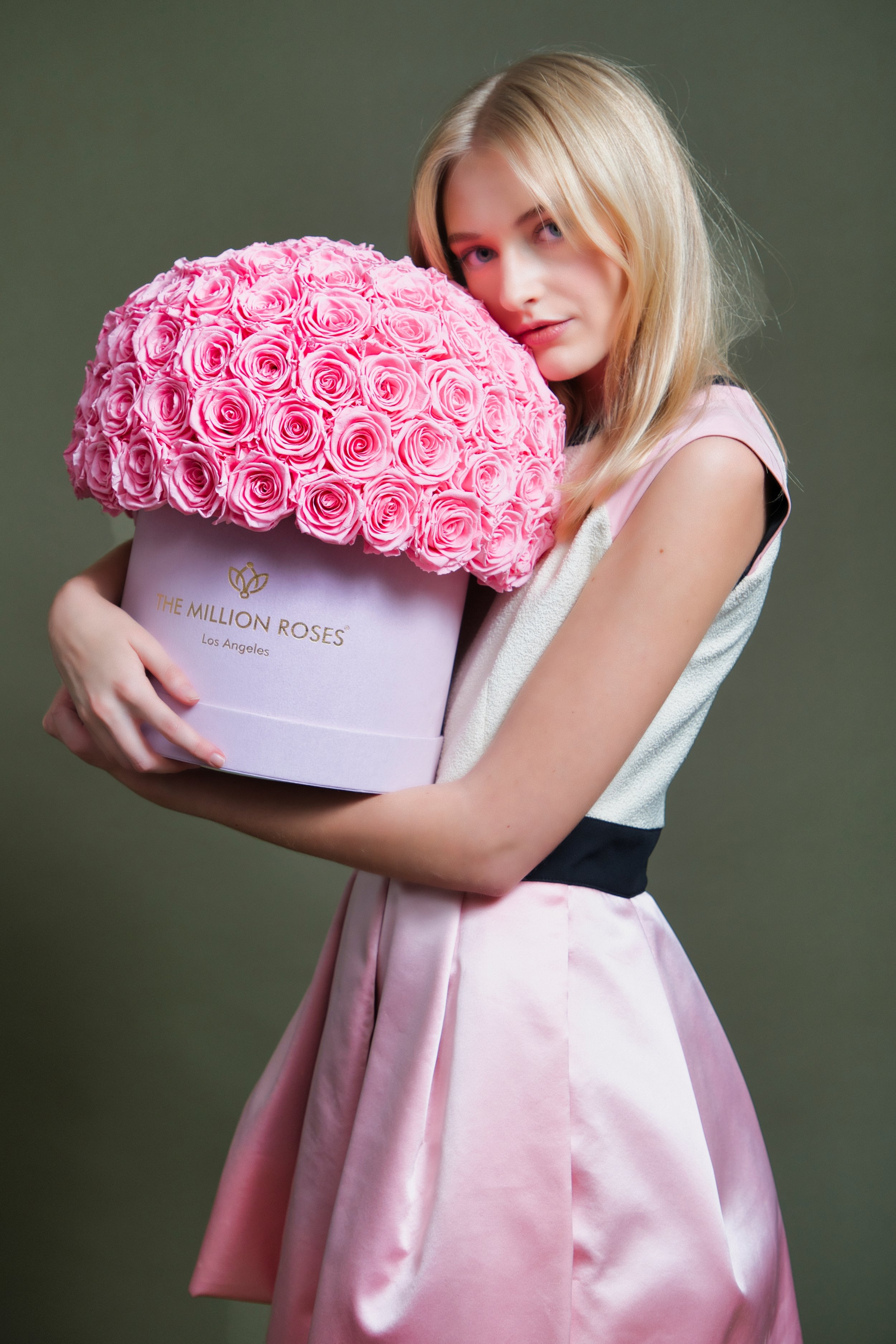 Photo model in white and pink dress presenting large pink The Million Roses flowers in pink box