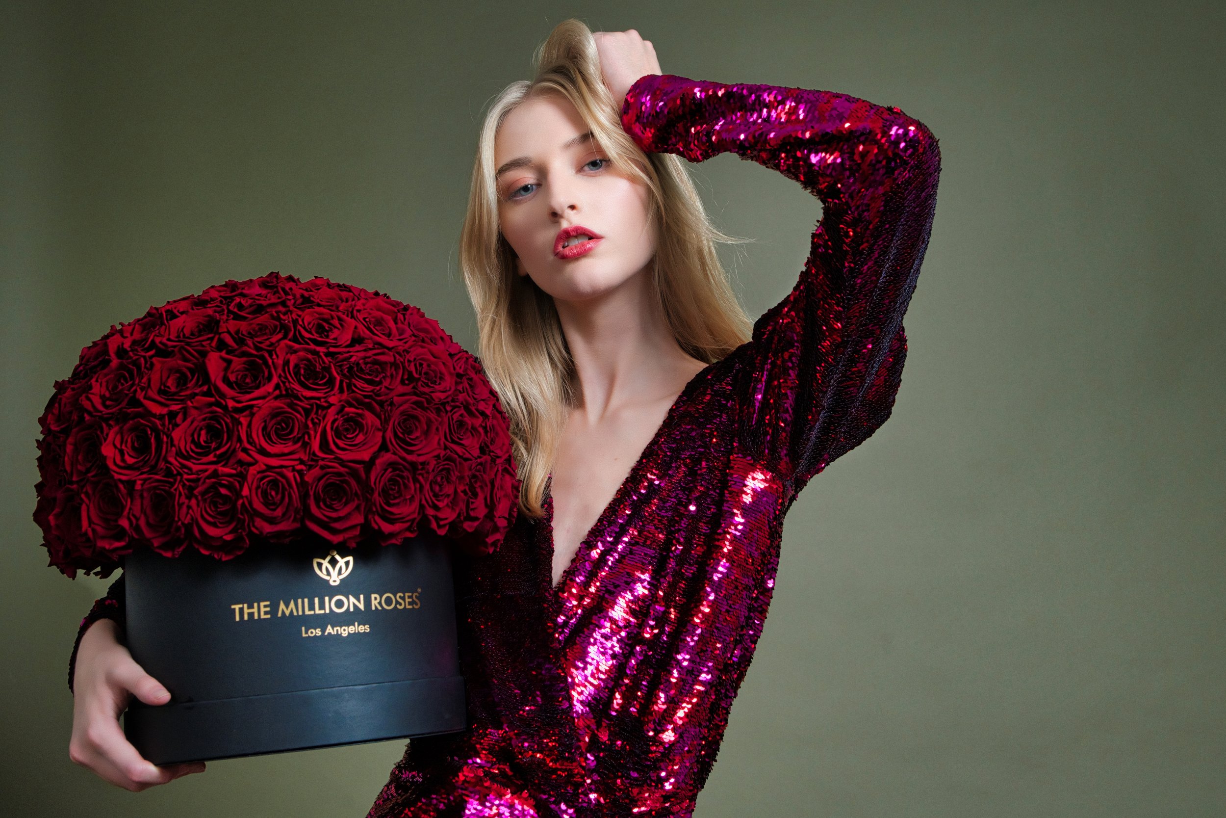 Photo model in shiny red dress presenting large red The Million Roses flowers in red box
