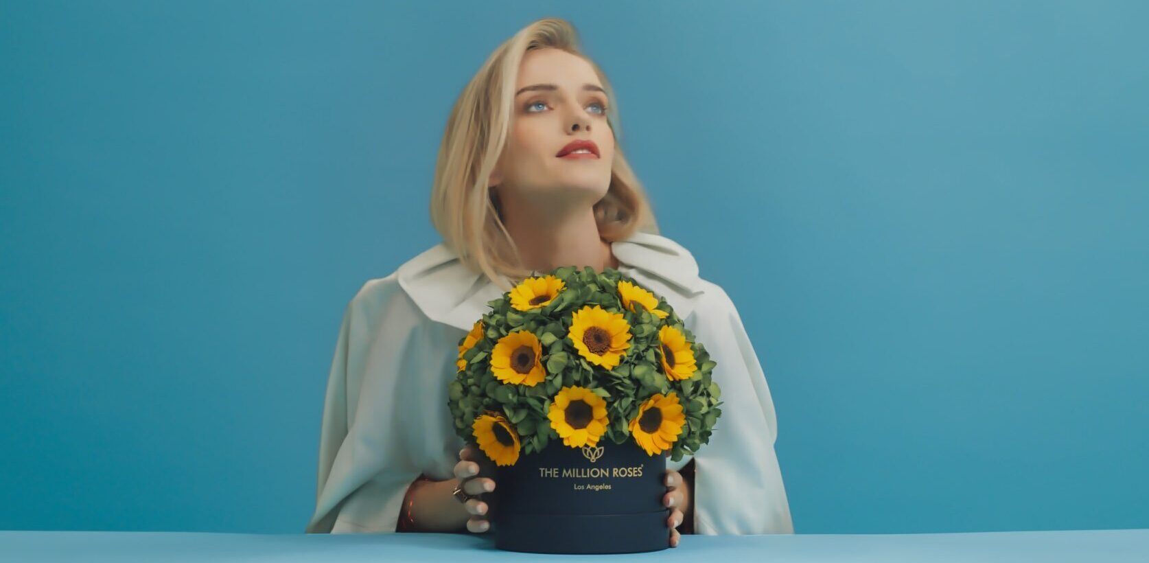 Photo model in blue background holding yellow The Million Roses flowers in gold box