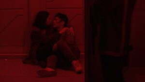 Two people hugging and sitting on floor in bright red lighting