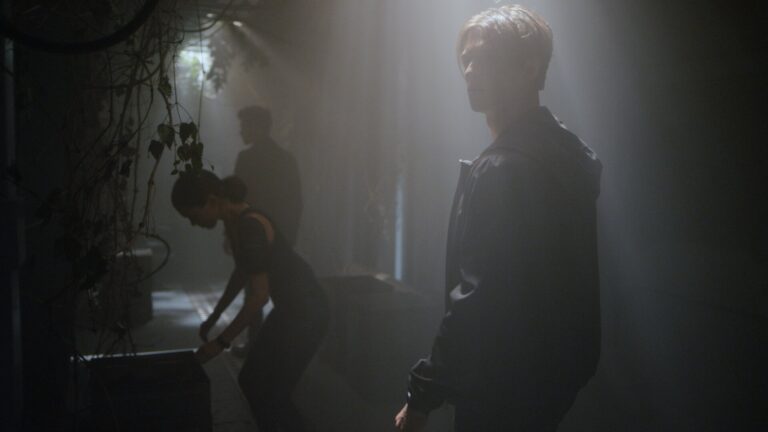 Three people walking through a dramatically lit hallway with shafts of light