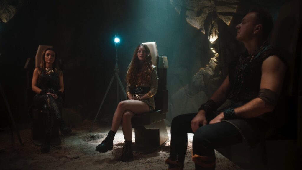 Dramatic scene of three people sitting in a cave on chairs with dramatic lighting