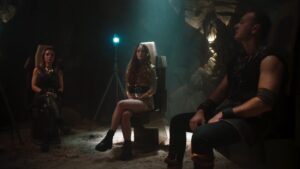 Dramatic scene of three people sitting in a cave on chairs with dramatic lighting