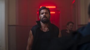 Manu Bennett walking down red lit corridor