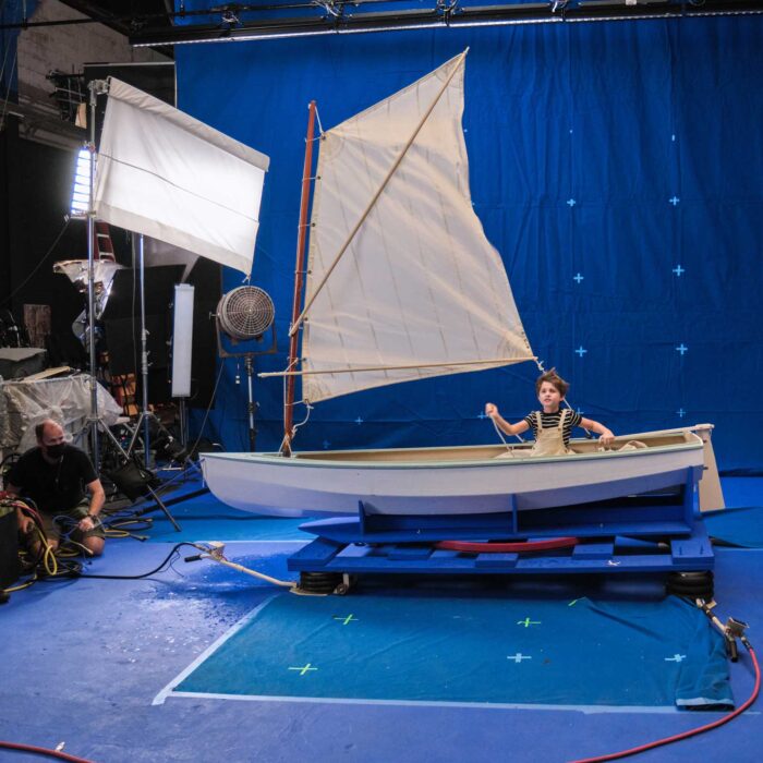 behind the scenes of a blue screen scene with boy operating a boat pretending to be out in the ocean