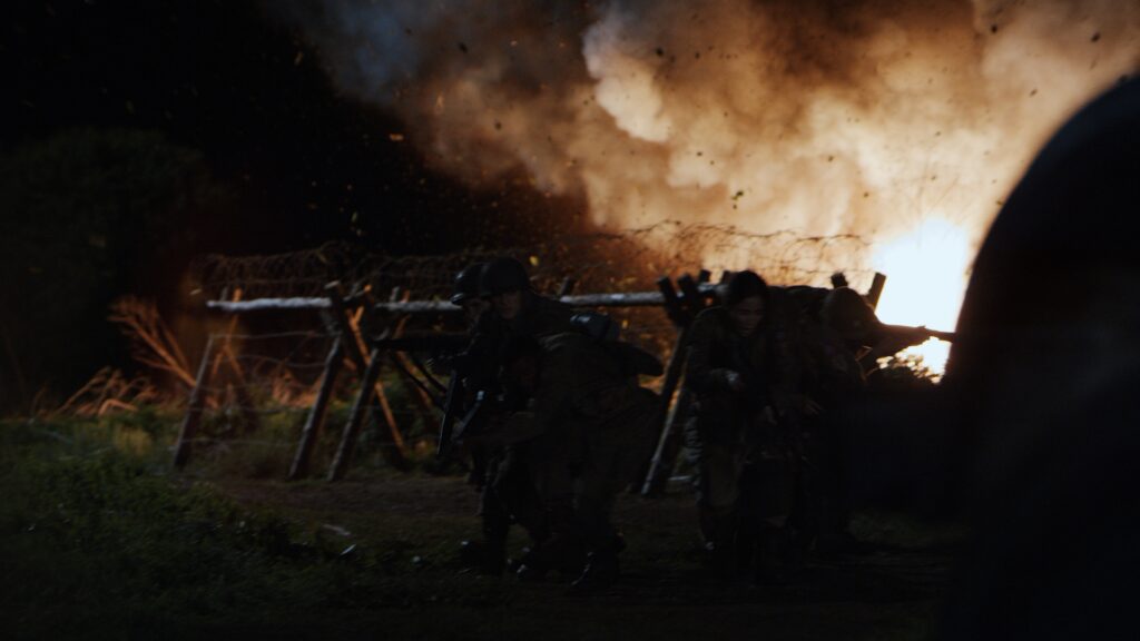 World War II movie scene with unit escaping explotion behind them at night