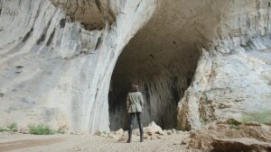 Wide shot of woman entering cave