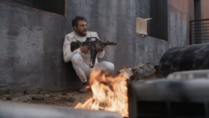 Marc Crumpton in spacesuit outfit and guns drawn hunched down in fight scene