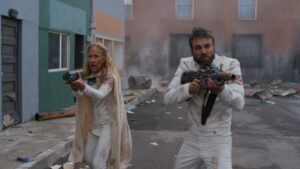 Erin Gray and Marc Crumpton walking gun blazed in worn town sci-fi street scene
