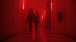 Two people walking down red warning light corridor