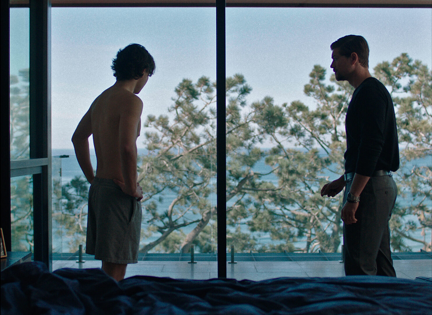 Carson MacCormac and Amadeus Serafini standing against a floor to ceiling window looking at trees