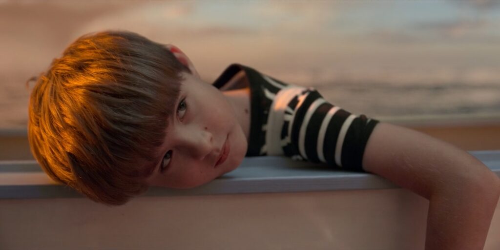 Boy leaning his head on the edge of a boat in golden sunlight