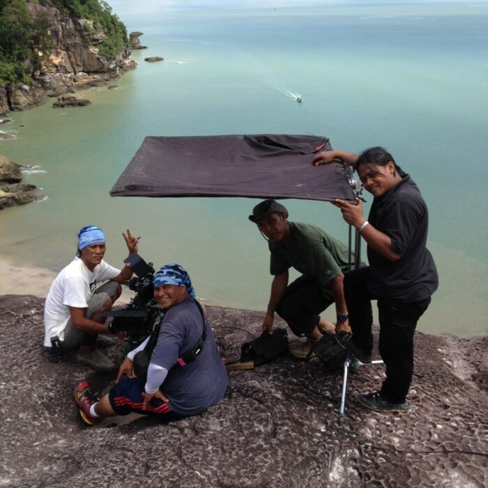 Film crew sitting at edge of cliff in Bako National Park Malaysia with floppy giving shade