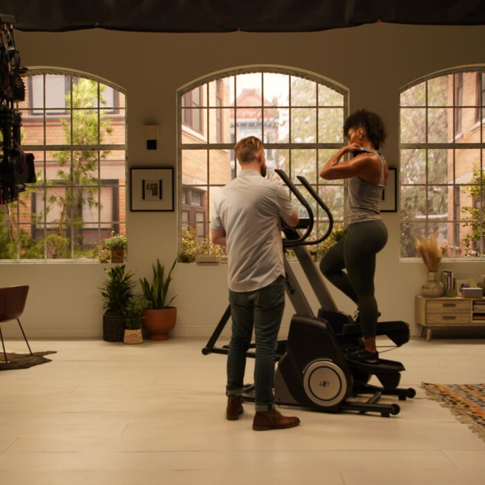 Brooklyn style loft apartment living room set with woman in treadmill and director giving directions.