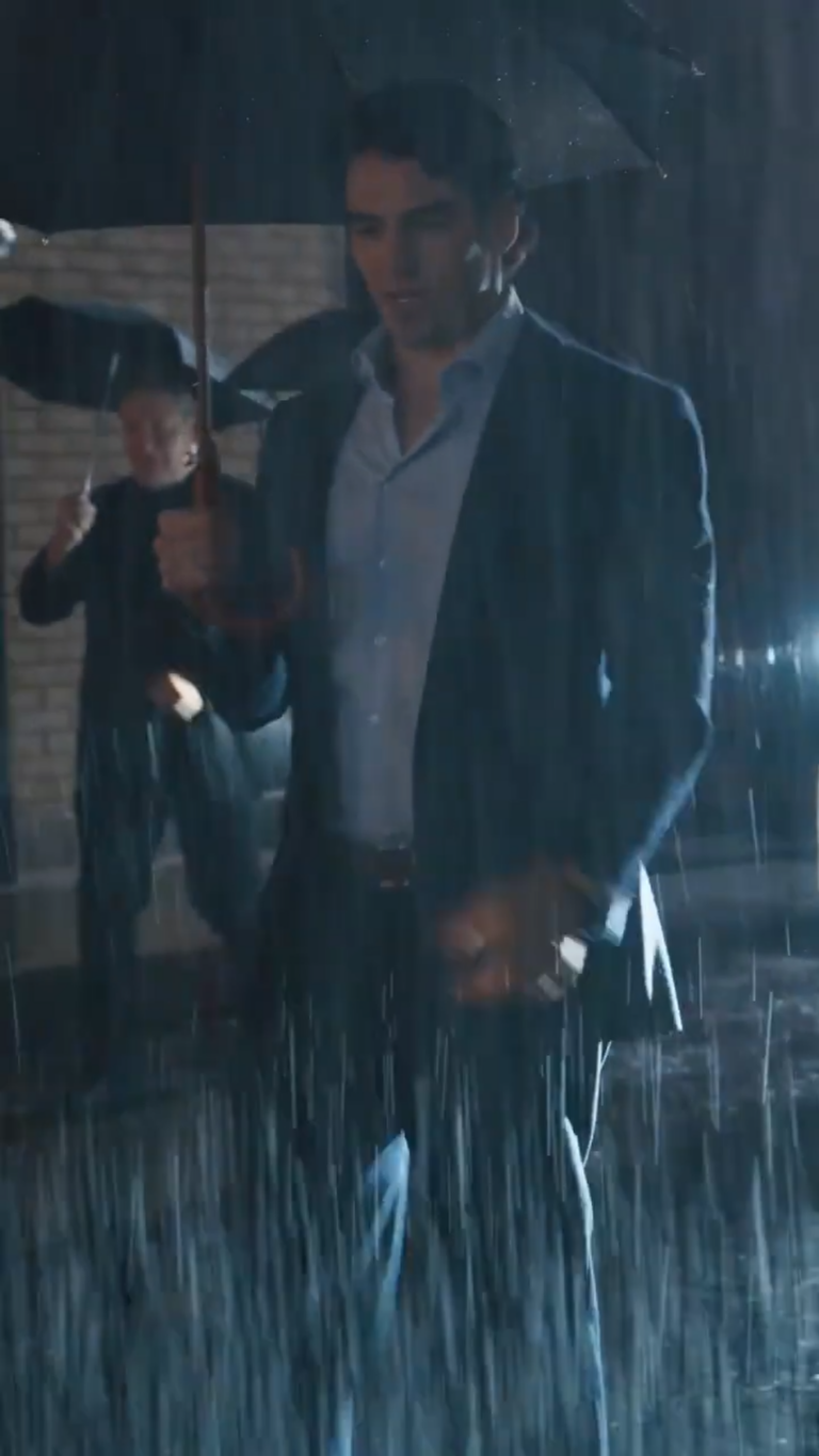 Actor Noah Fearnley walking in rain at night holding an umbrella